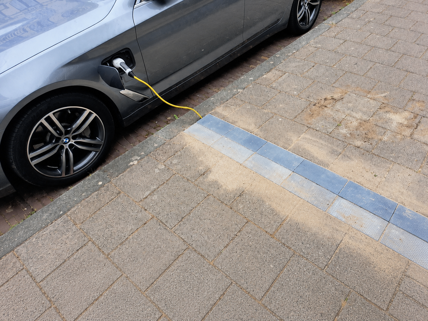 Elektroauto am Straßenrand mit Ladekabel, das über eine bündige Kabelrinne im Gehwegpflaster verläuft.