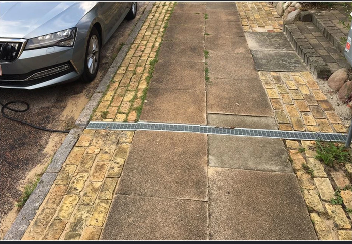 Quer im Gehweg eingelassene Kabelschiene neben einem am Straßenrand geparkten Fahrzeug