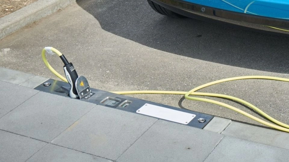 In den Bordstein integrierter Rheinmetall-Ladepunkt mit eingestecktem Ladekabel zum Elektroauto.